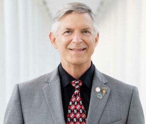 headshot of Larry Feldman in a grey suit, black shirt, and red and black tie