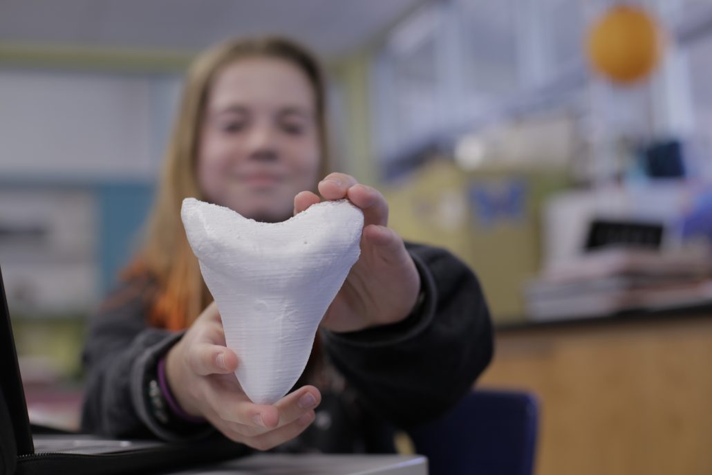 Student holding up a 3D printed shark tooth.