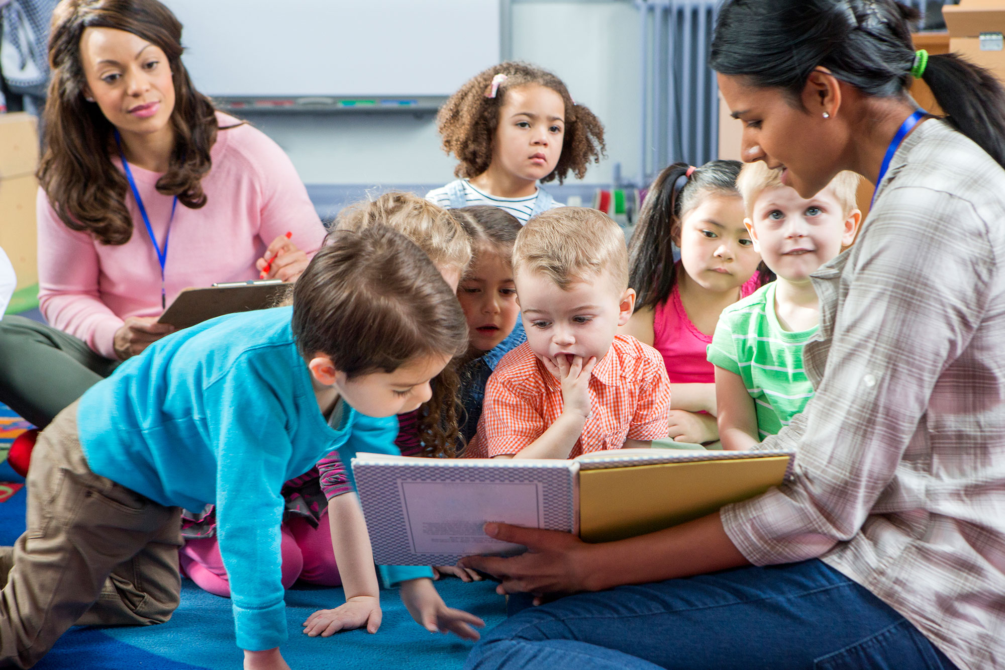 A teacher coach observes a teacher reading to a classroom of children.