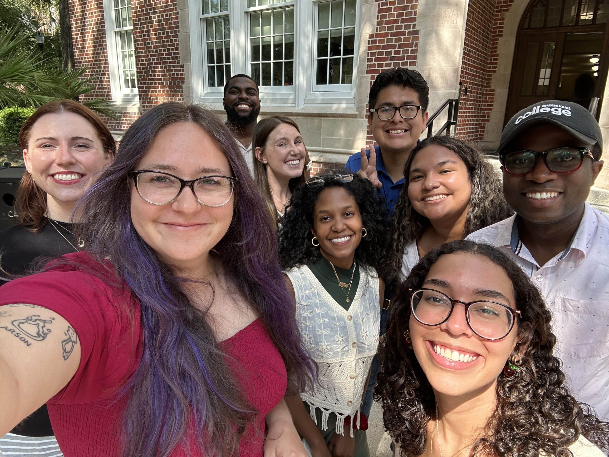A selfie shot of on-campus Student Personnel in Higher Education master's students outside UF's Norman Hall. They are all smiling at the camera.