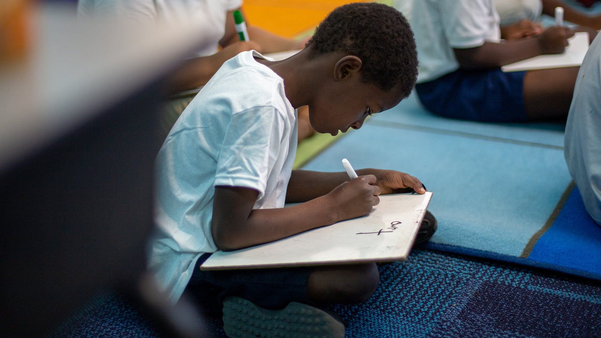 Student sitting on the floor and writing on a whiteboard. 