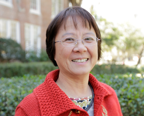 Danling Fu is smiling outside in this posed photograph. They are wearing a red sweater and glasses.