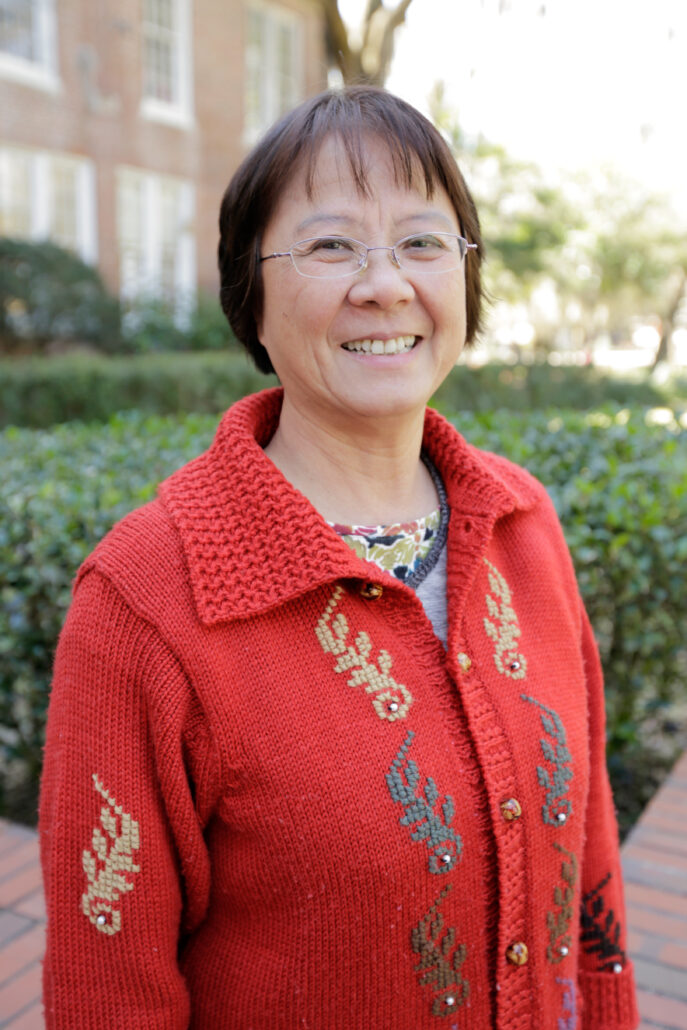 Danling Fu is smiling outside in this posed photograph. They are wearing a red sweater and glasses.