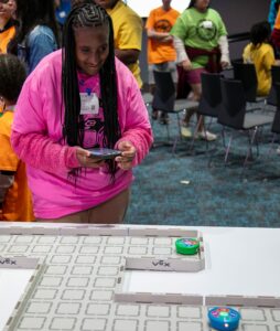 student in a pink shirt interacts with Vex robotics devices on a table