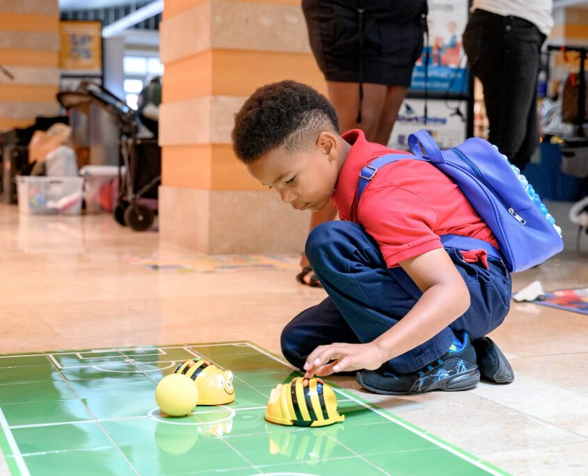 a child interacting with a yellow and black robotics device on a green mat on the floor