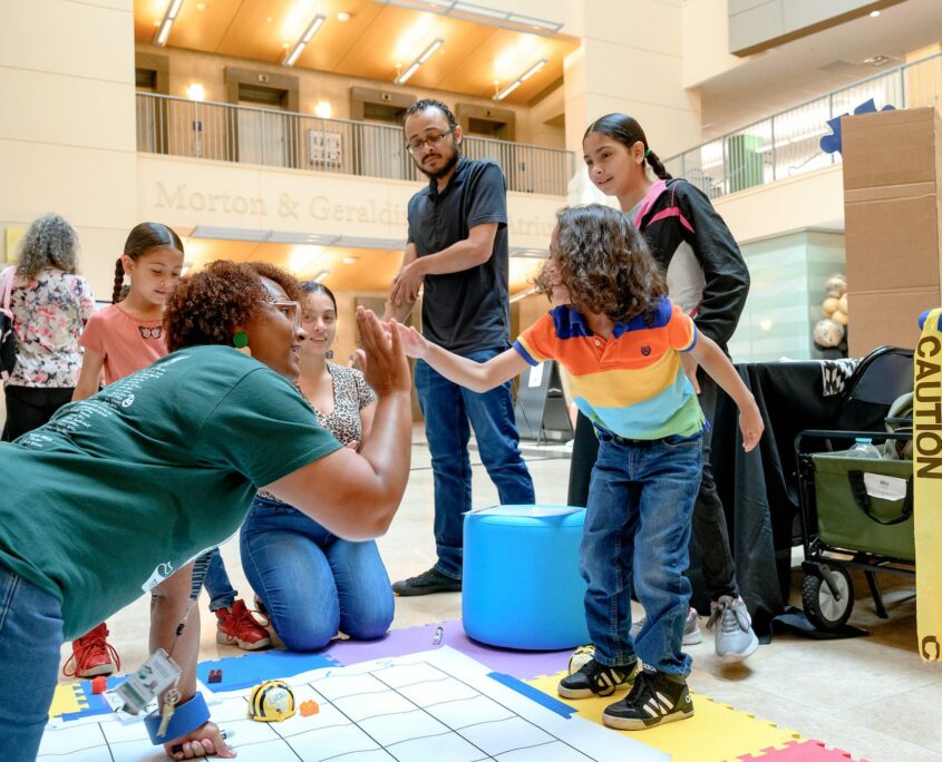 A student is high fiving an adult while family members look on in the background.