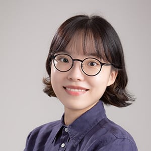 Portrait of a person with chin-length dark hair wearing a dark blue button-down shirt, posed against a light gray studio background.
