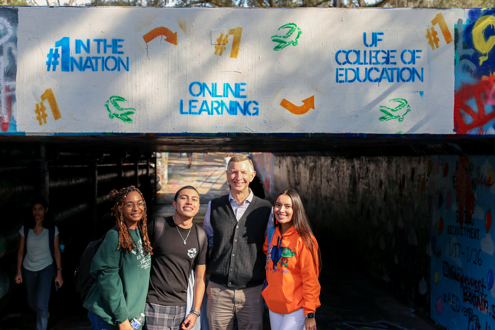 Dean Good smiling in front of a graffiti wall with three students.