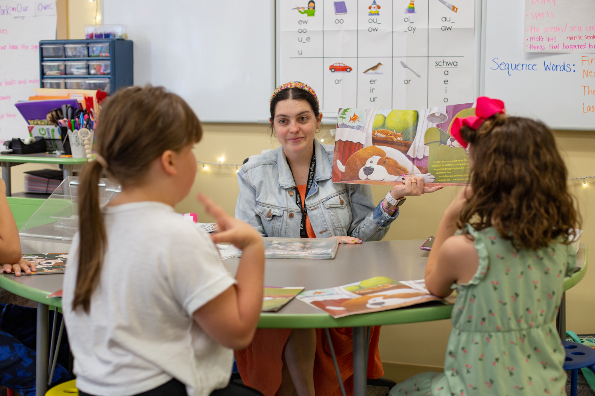 A teacher reading a picture book to two young students at a table.
