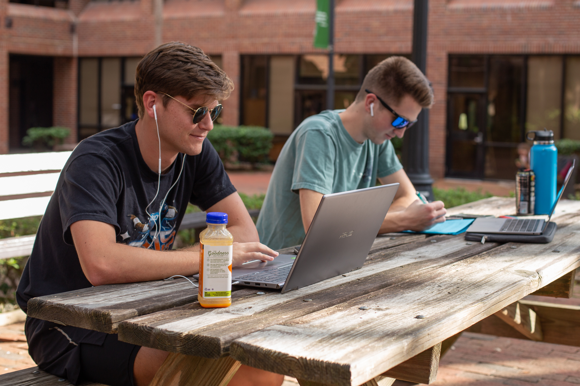 Two students on laptops sitting outdoors at a picnic table