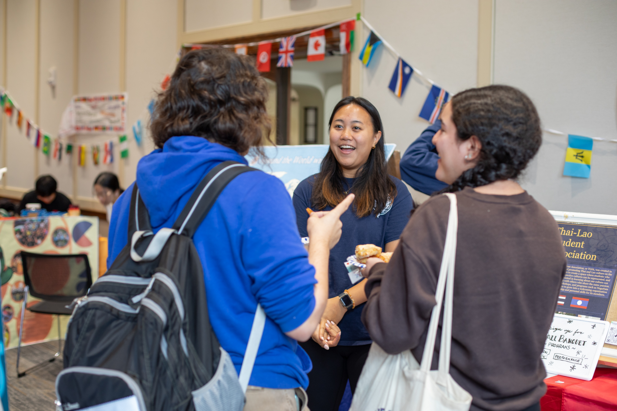 Group of students talking at the UF College of Education International Fair. There are flags from many countries on the wall.